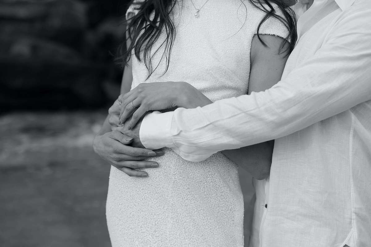 black and white photo of pregnant lady with husband holding belly.
