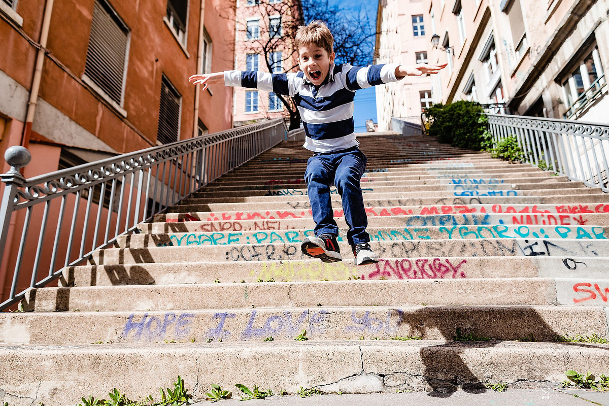 Photographe Famille Lyon Reportage Documentaire - Enfant sautant joyeusement les marches à la Croix-Rousse dans une séance photo dynamique à Lyon