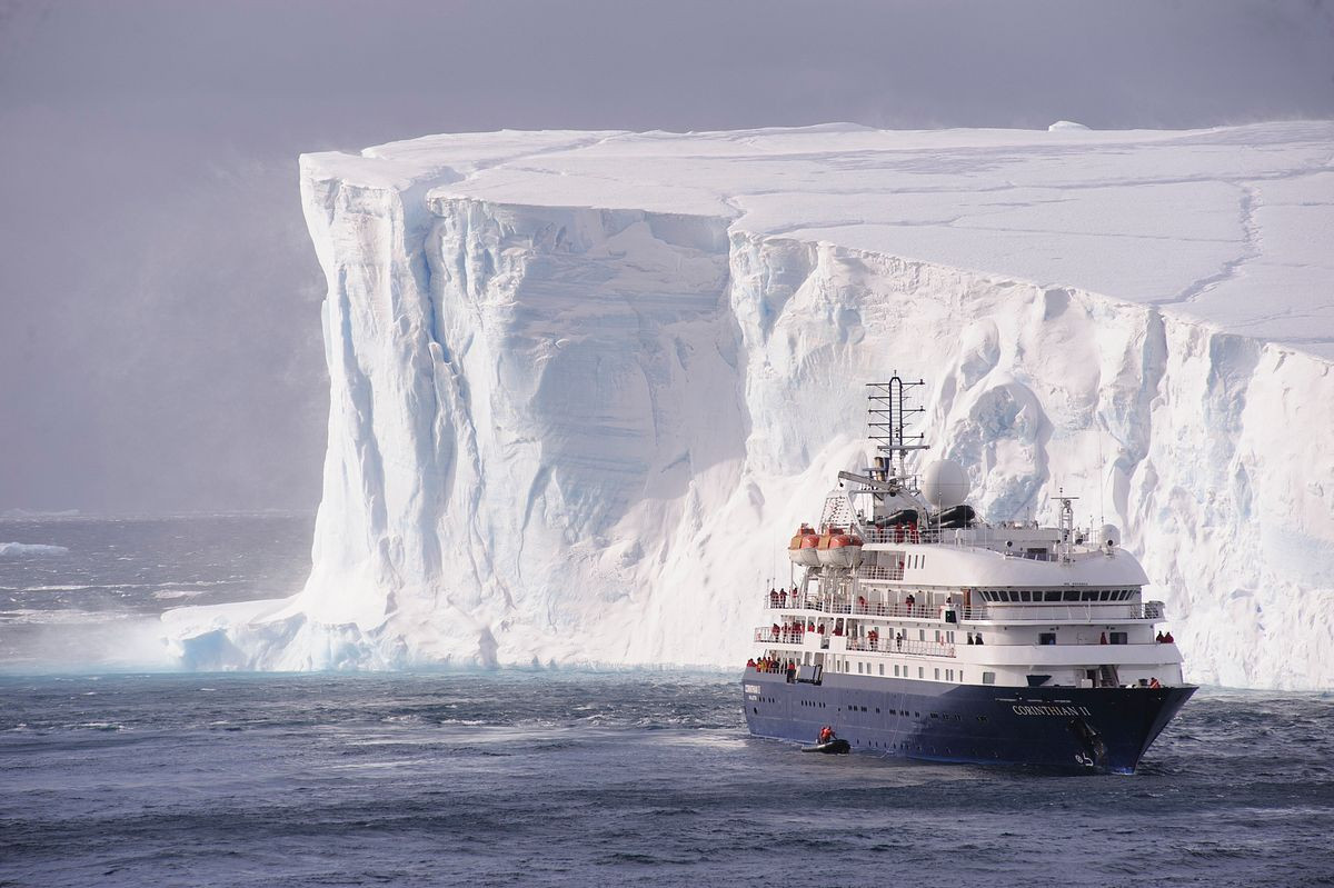 Small cruise ship beside massive tabular iceberg in Antarctica