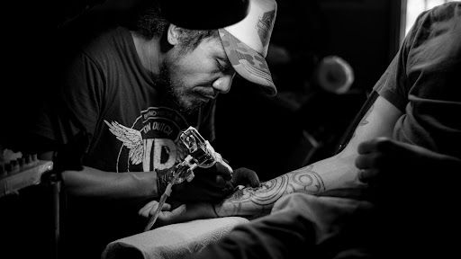 Artista del tatuaje entintando en el brazo derecho