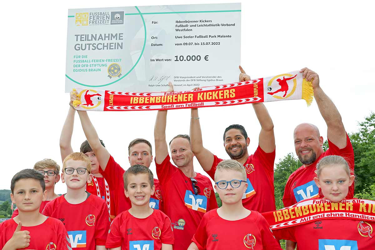 Glückliche Kinder und ehrenamtliche Trainer der Ibbenbürener Kickers erhalten den Teilnahmegutschein für die Fußball-Ferien-Freizeiten 2022 von Sören Storks und Christian Gittelmann.