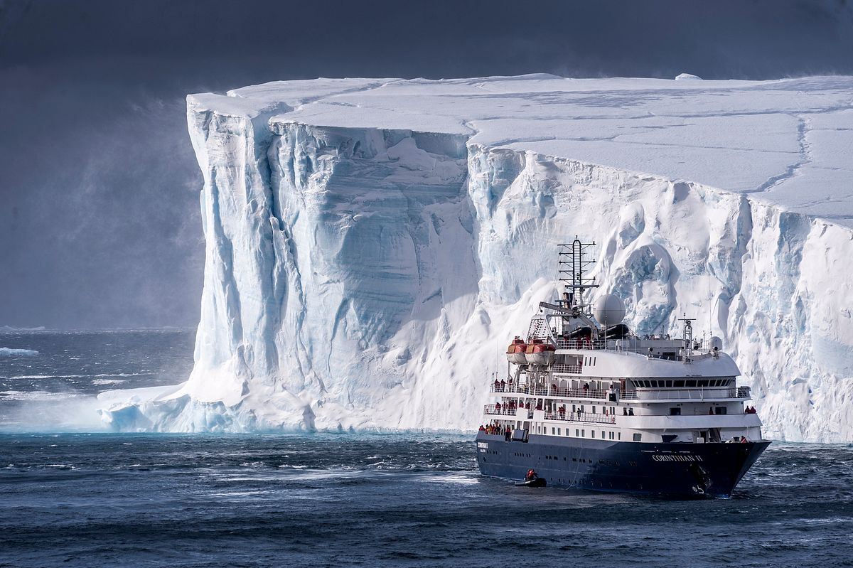 Small cruise ship beside massive tabular iceberg in Antarctica
