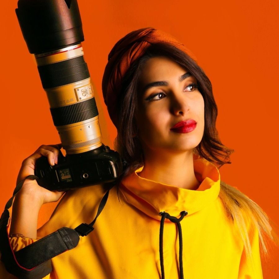 Modefotograaf met camera op een oranje achtergrond