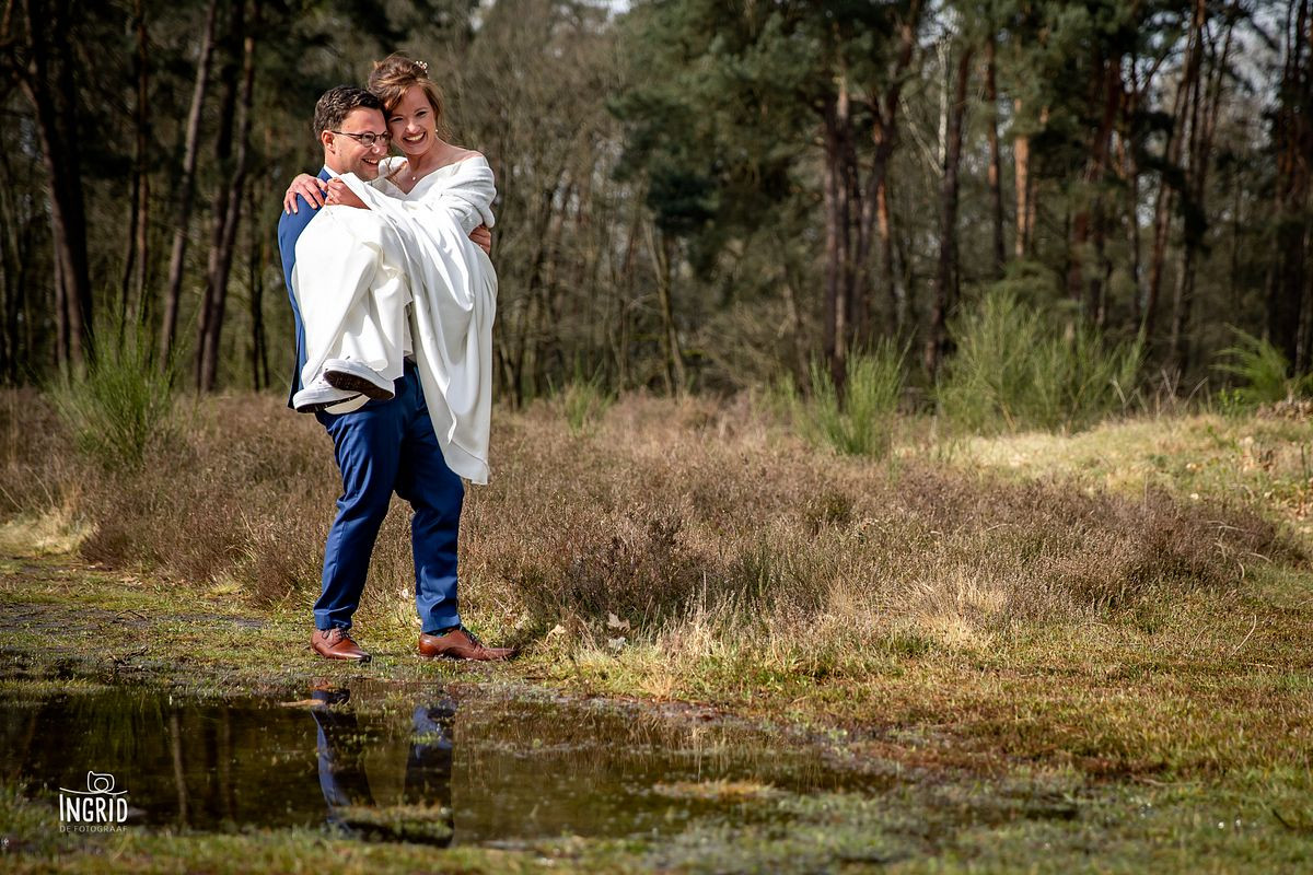 Bruidegom tilt bruid over plas water heen in natuurgebied tijdens fotoshoot